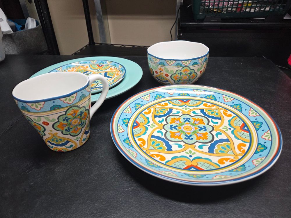 A teal charger plate with a decorated salad plate on it at top, right is a decorated bowl, bottom is a decorated dinner plate, left is a decorated mug