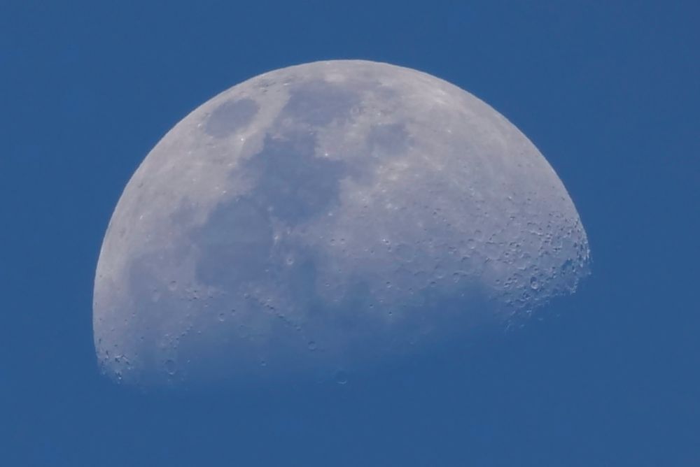 Waxing gibbous moon, about 56% seen, in the late afternoon blue sky.