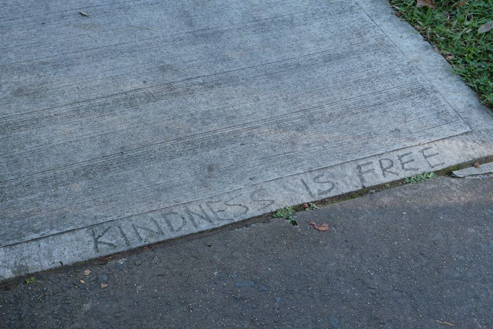 Footpath with the words 'Kindness is free" in capital letters scratched into it.