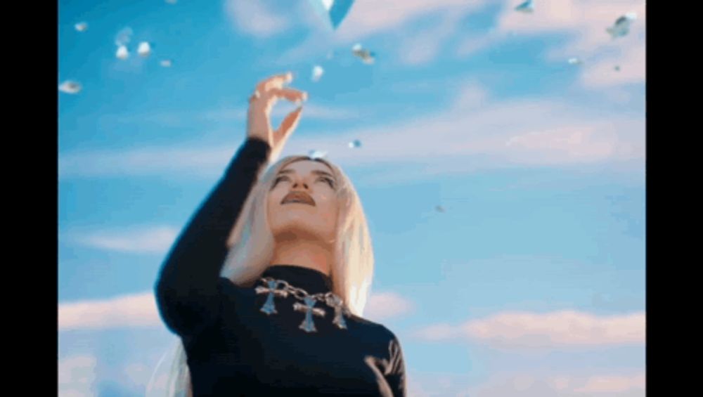 a woman wearing a black turtleneck and a cross necklace looks up at the sky .