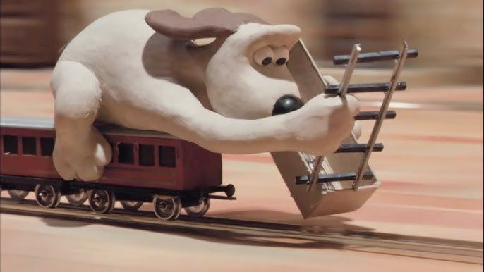 A screencap of the dog gromit laying down railway line in front of the fast-moving train on which he is sat.