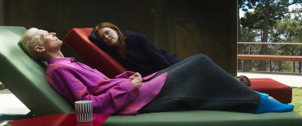 Julianne Moore (au deuxième plan) est allongée sur un transat rouge en regardant Tilda Swinton (premier plan) qui est en train de faire la sieste sur un transat vert 