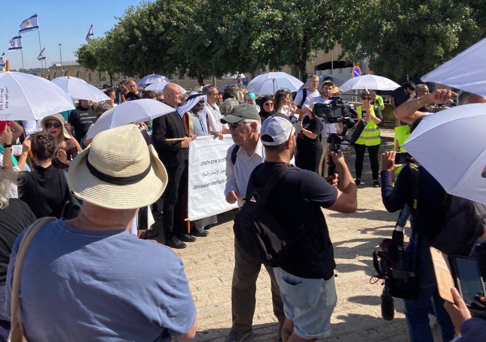 Photo-op of the Interfaith March. A priest, a bedouin Sheikh, a female Rabbi and a Muslim woman in a blue-green Hijab can be seen holding a banner.