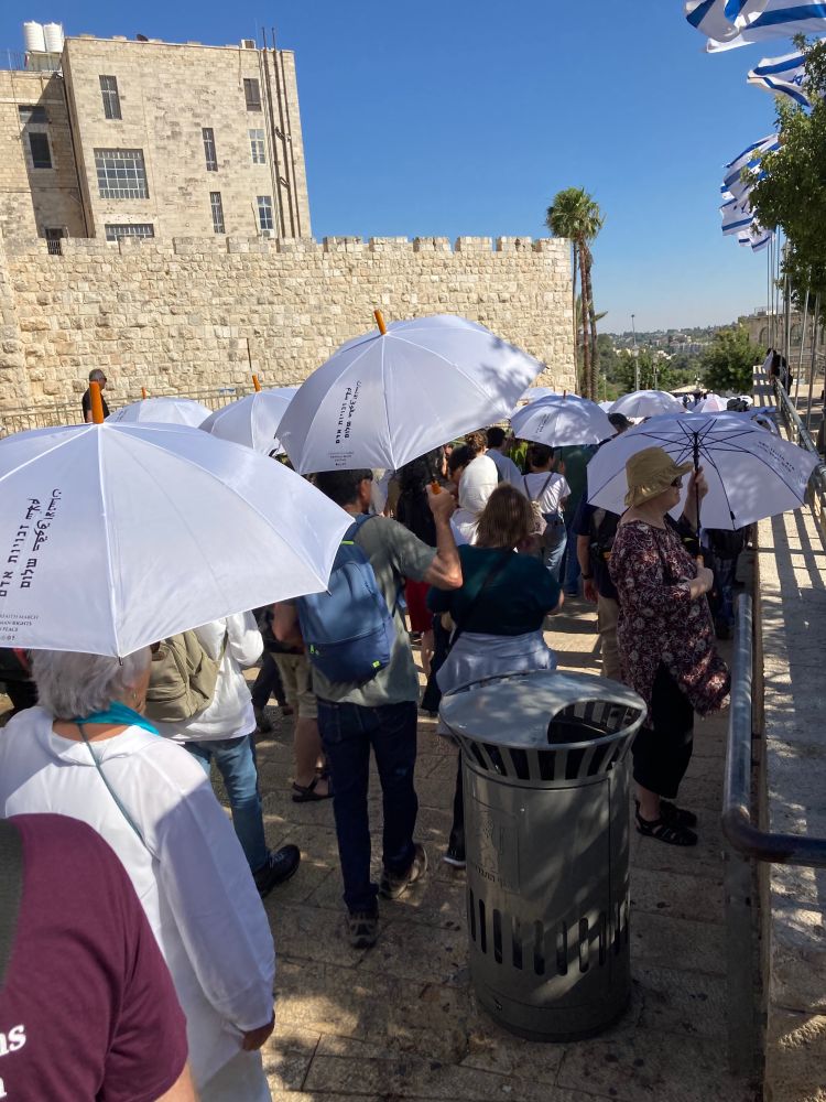 Marchers along the Old City walls. Many of them are carrying white parasols. The parasols carry writing in Hebrew and Arabic saying "peace" and "human rights"