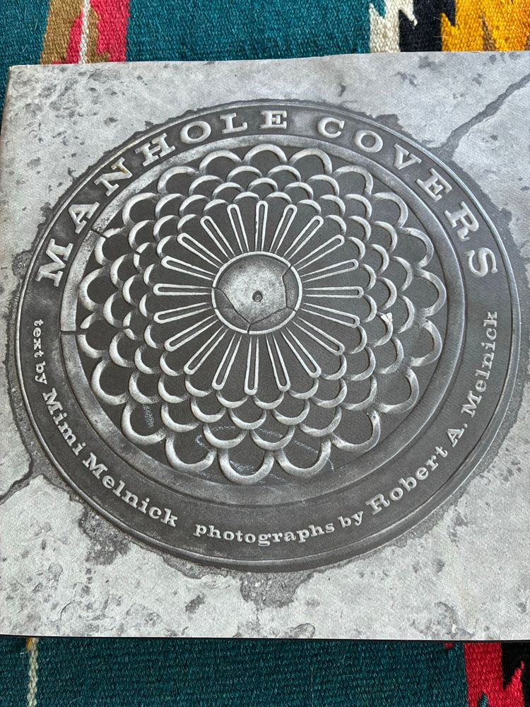 Hardcover book titled “manhole covers” with a black and white photo of a manhole cover on concrete 