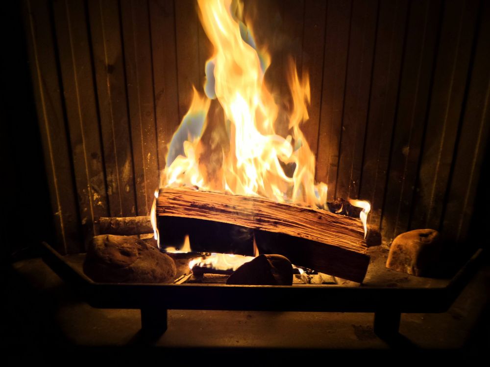 Un trozo de tronco partido por la mitad encendido en la chimenea de casa. La llama es amarilla y naranja y el tronco parece que no arde. Calorcito.