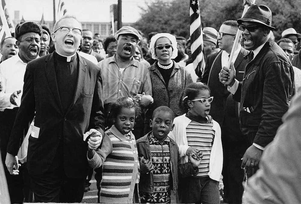 A black and white photo of James Reeb marching with Ralph Abernathy, Martin Luther King Jr., Coretta Scott King, and others.