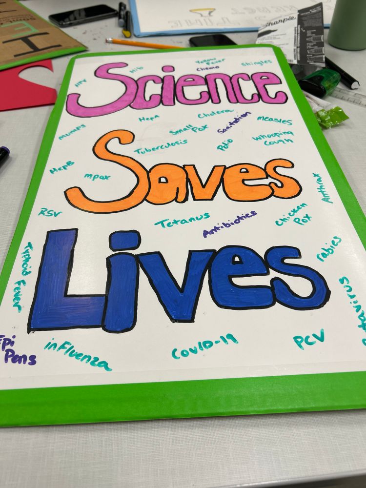 A protest sign that in large words states “Science saves lives” with different diseases that have vaccines scattered around the larger words 