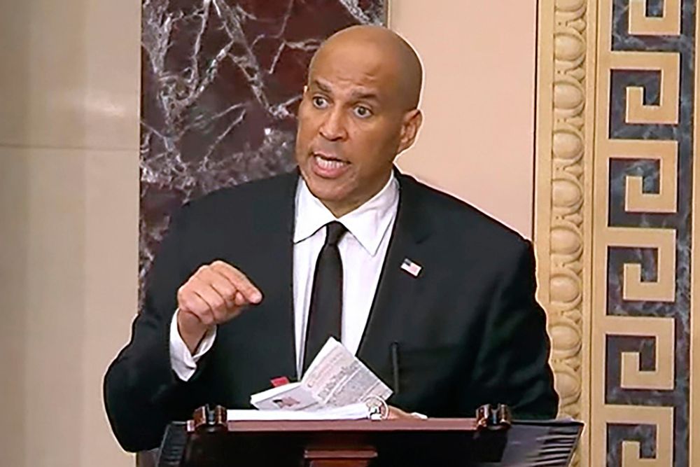 Sen. Cory Booker, standing at a podium holding a pocket copy of the US Constitution. 