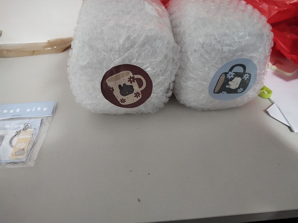 Duas canecas embaladas em plástico bolha com adesivos identificando as canecas azul e vermelha 