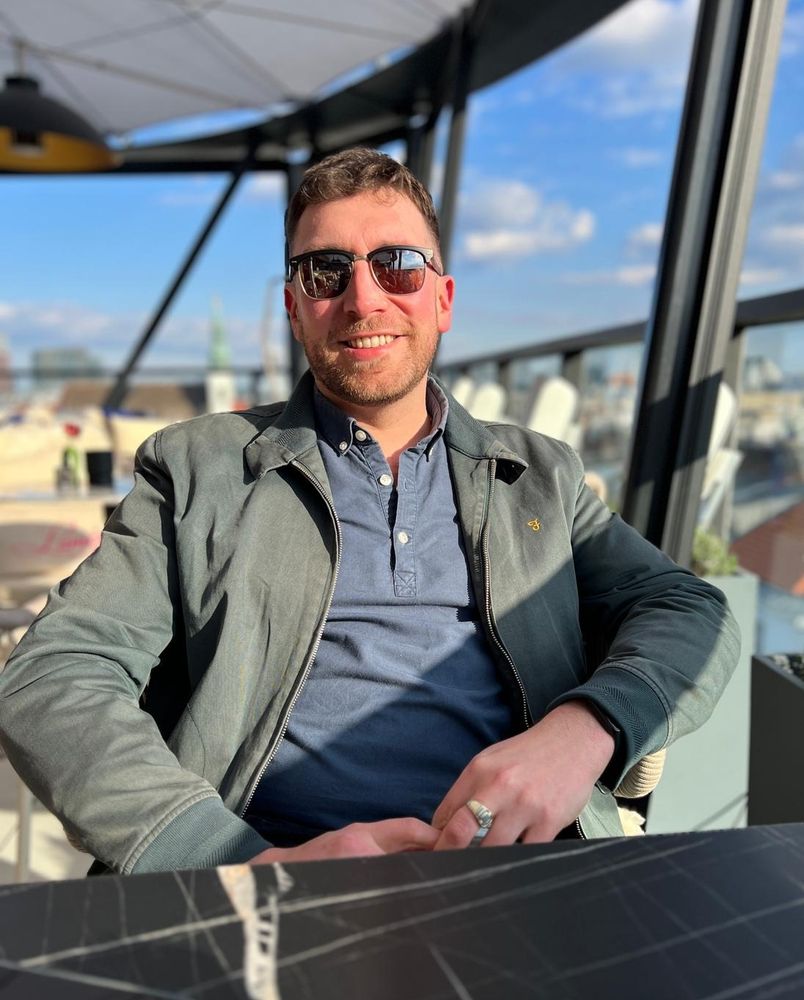 Man in sunglasses smiles at the camera on a rooftop bar 