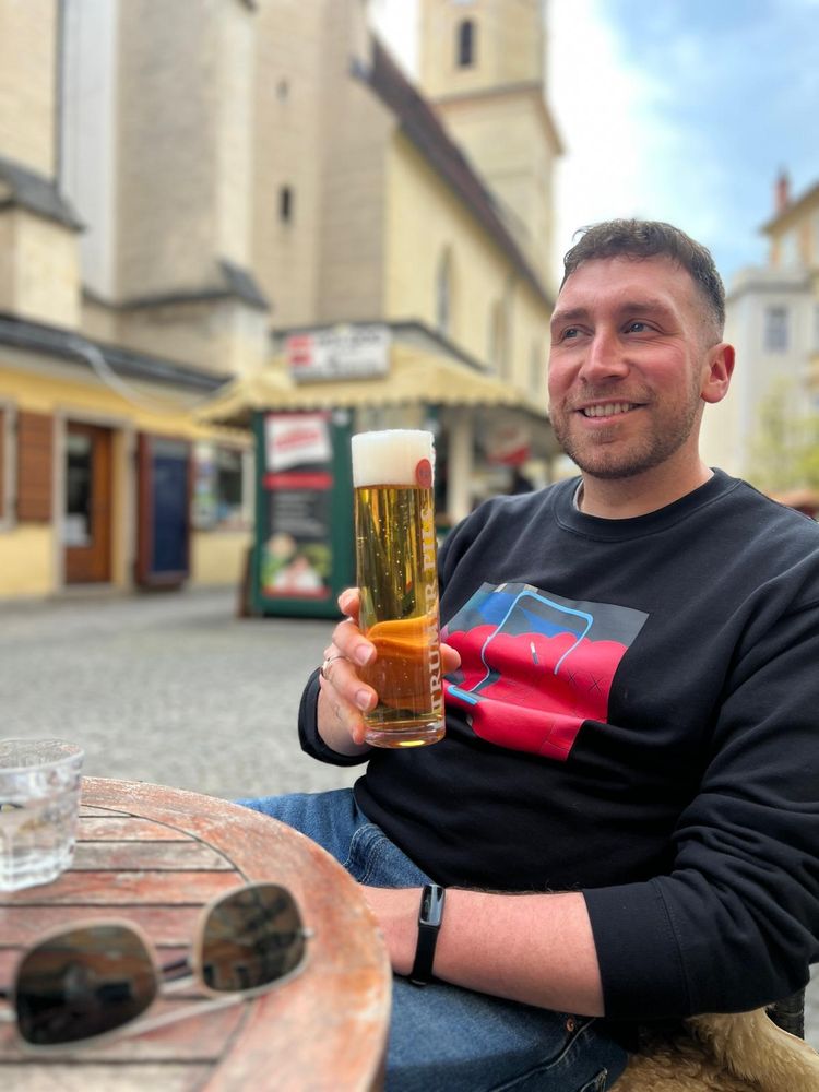 Man holds a beer and smiles in an Austrian courtyard 