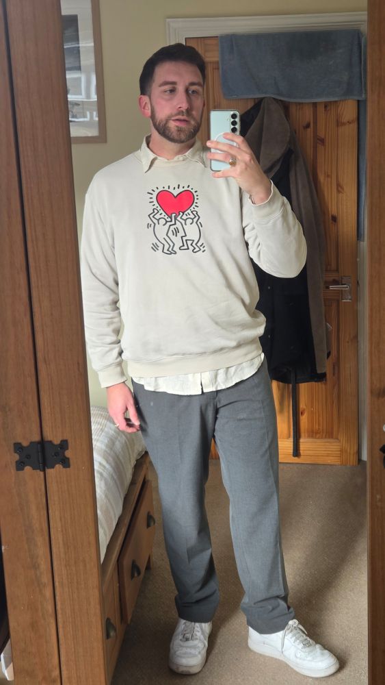 Man in white trainers, grey trousers and a dream Keith Haring top takes a selfie in a mirror. 