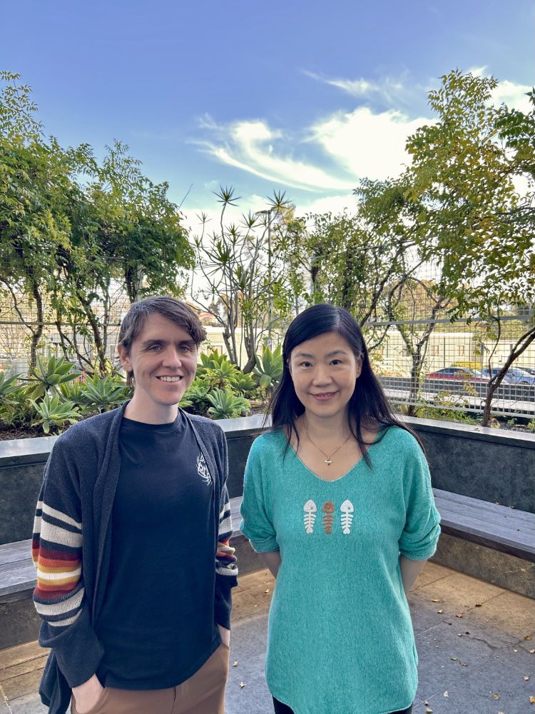 A photo of Ryan on the left, and Jin on the right, outside with trees and a blue sky.