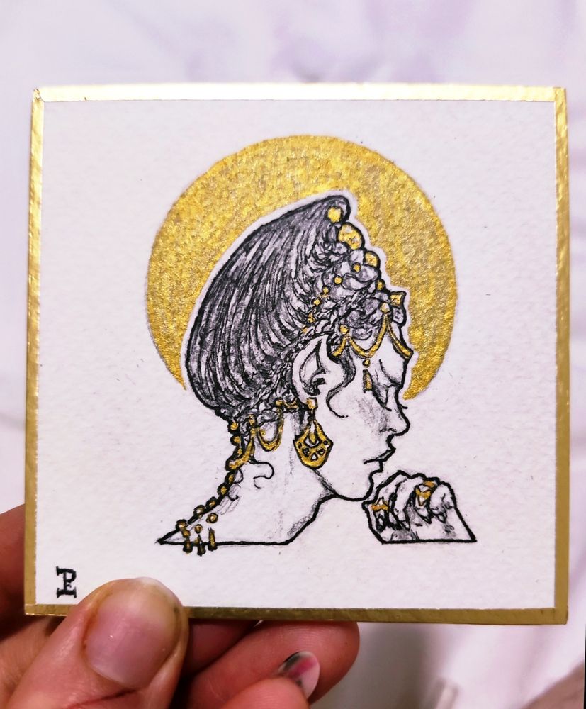 Photo of a hand holding a small bust illustration of T'Pring from Star Trek made with graphite, black and gold ink on a shikishi paperboard. She's on profile, her eyes closed, and her hand flexed below her chin. She's wearing extensive gold Vulcan jewellery consisting of geometric earrings, several earrings and accessories on her head, golden pearls of different sizes and small gold chains in a composition reminiscent of a sort of crown or diadem. She's framed by a gold halo in the background.