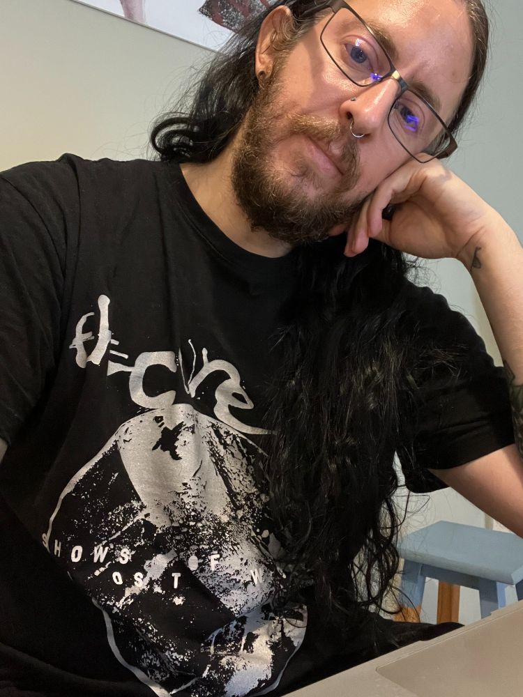 Dark-haired man with a beard and glasses, with a Cure T-shirt on