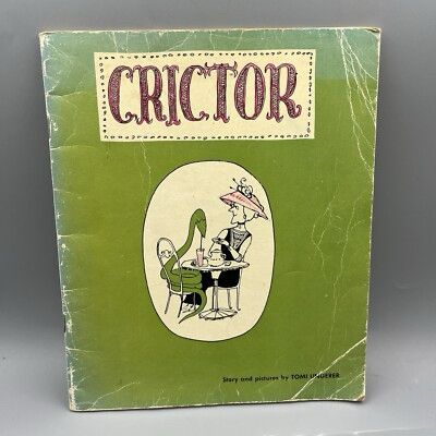 An old green children’s paperback book called Crictor. On the cover, the titular character, a green boa constrictor, sits at a Parisian cafe table drinking a drink with a straw. Opposite him is a fashionable elderly lady stirring tea. 