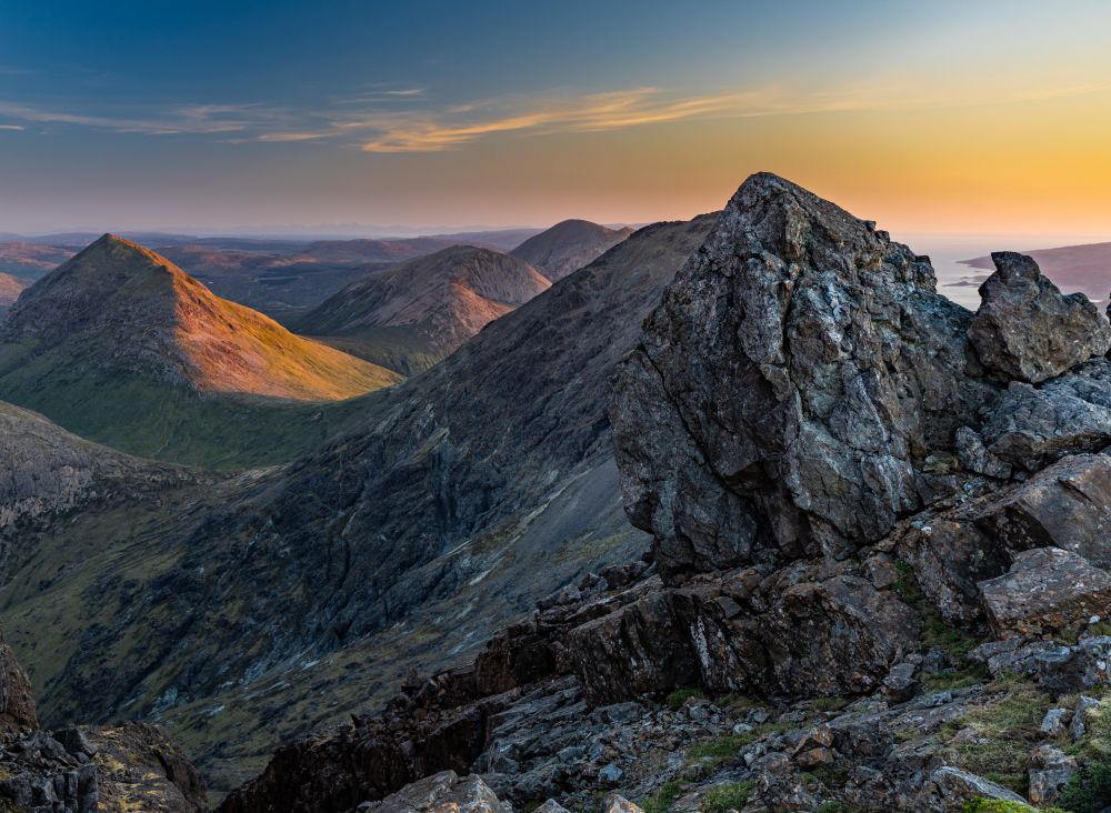 The view from the summit of Mount Bla Bheinn, Isle of Skye, Scotland. The image is wide angle view of mountains leading to the ocean facing North North West. This image was taken just as the sun rose features a secondary peak just below the summit.