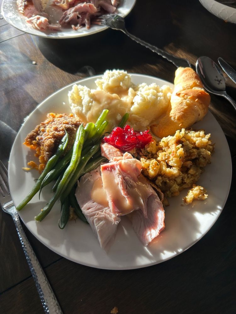 Dinner plate with turkey, mashed potatoes, green beans, sweet potato casserole, and crescent roll.