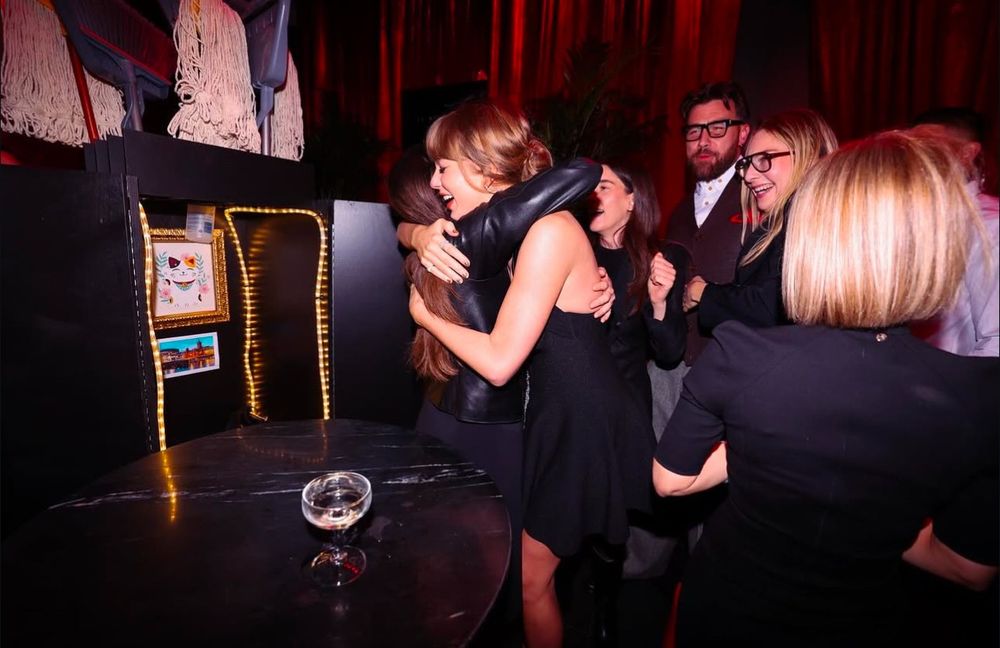 Taylor Swift hugging a woman in front of a group of people and her cleaning cart.