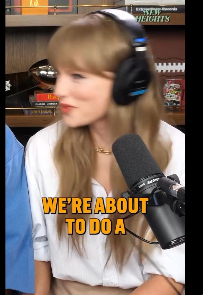 Taylor Swift with headphones and a white top sitting next to Travis Kelce (off screen)"we're about to do a"...