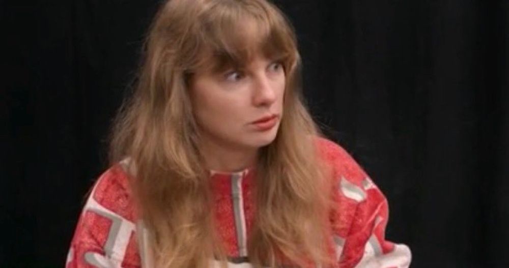 Tay Swift in red sweater with wide eyes looking surprised at someone off screen.