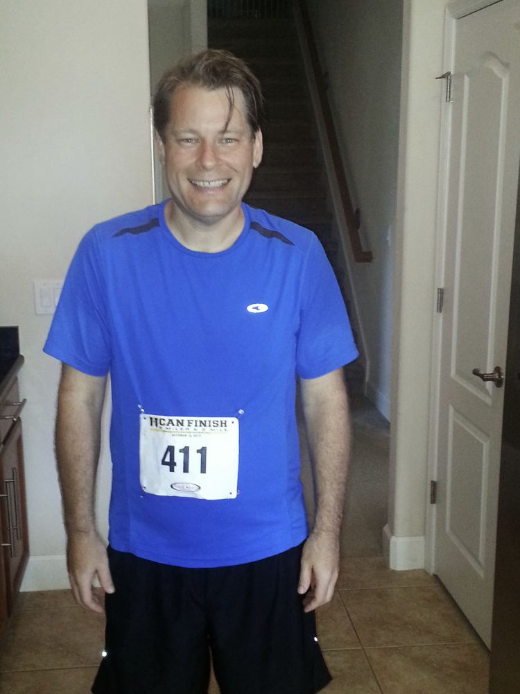 A thin man in a blue shirt wears a "U can finish" racing bib.  He looks much healthier than the previous photo.