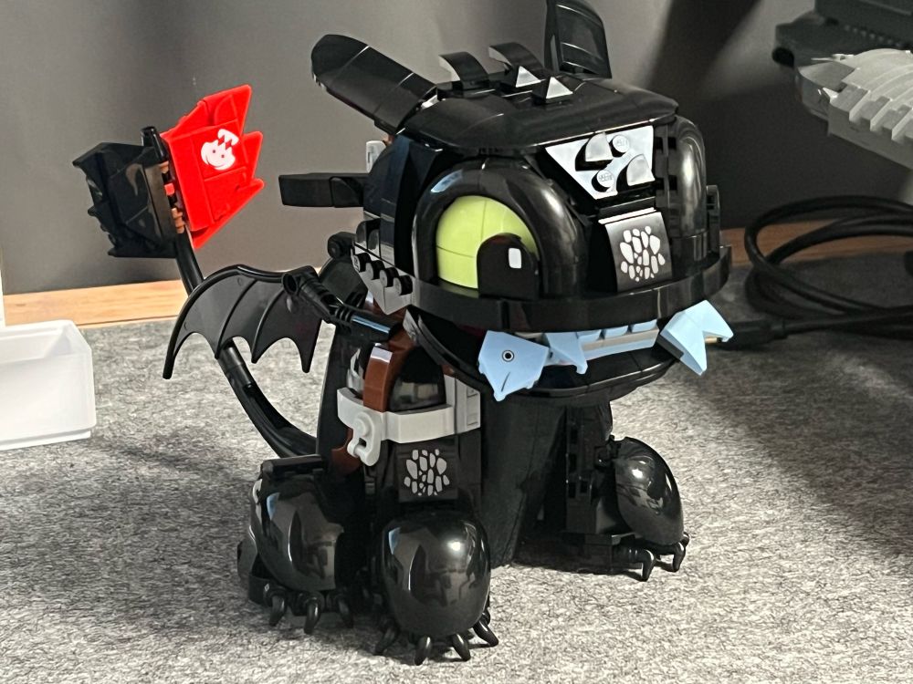 Lego version of the Nightfury dragon toothless sitting upright and a fish in his mouth