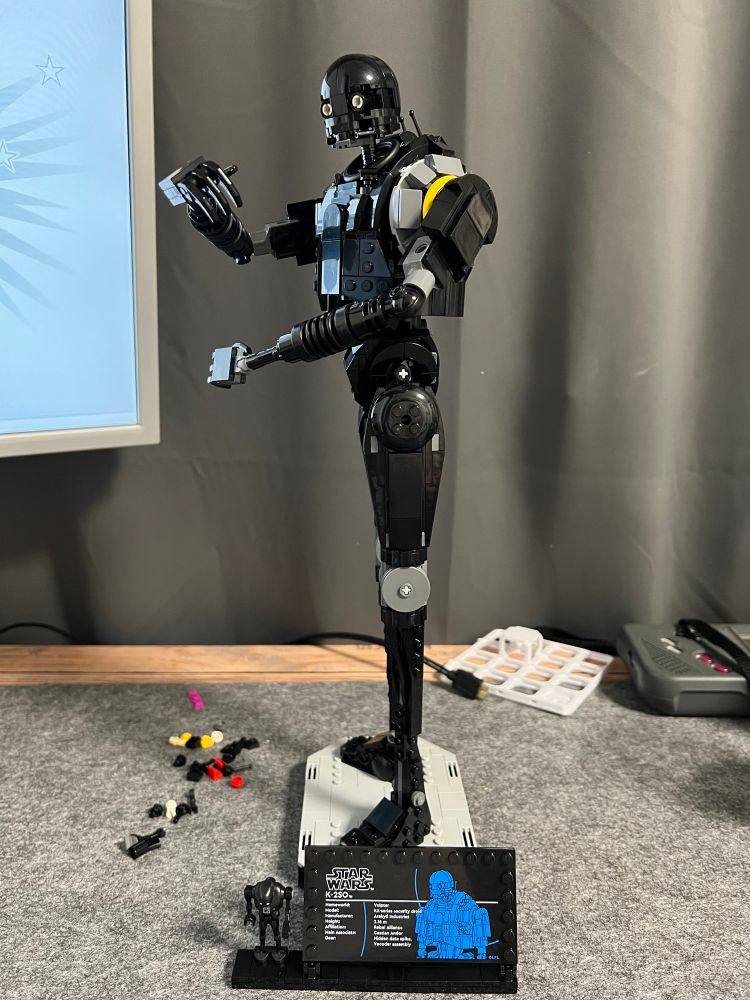 Brick build (Lego) K-2SO from Star Wars left side view. His head is turned left towards the camera. Both arms are raised one to belly and one to chest height 