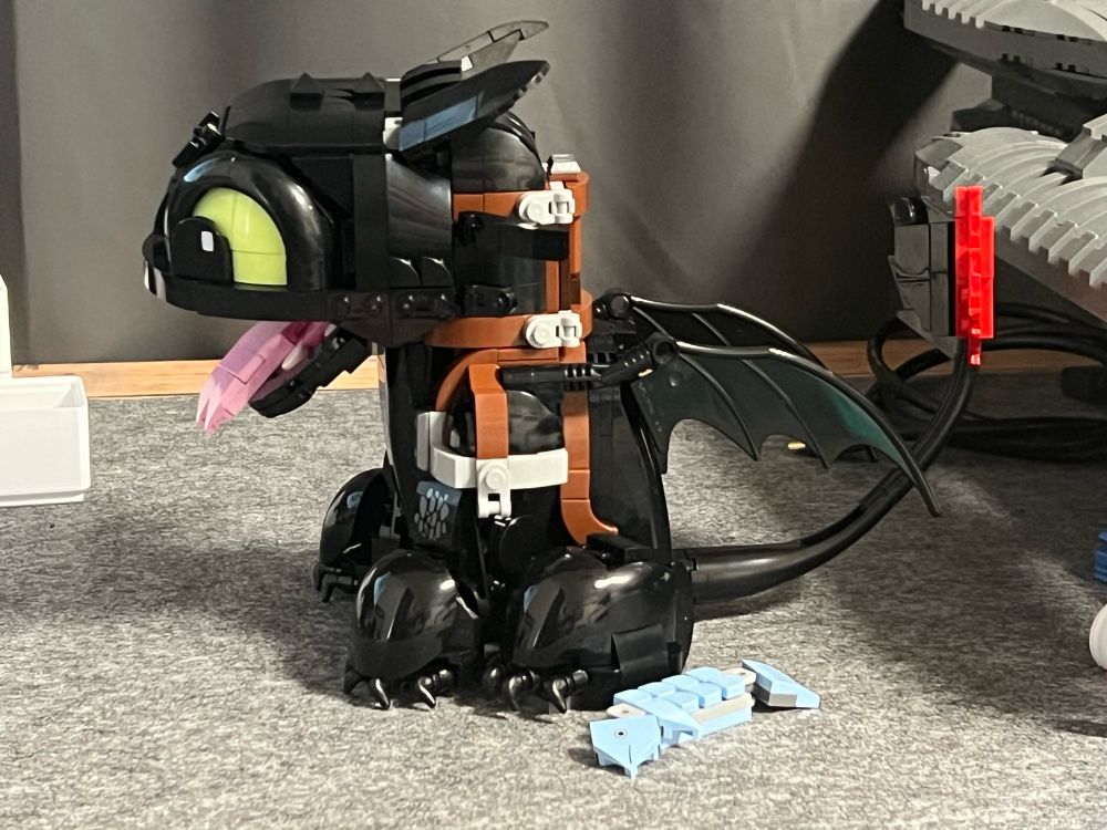 Seide View of the Lego version of the Nightfury dragon toothless sitting upright, open mouth and fish next to him
