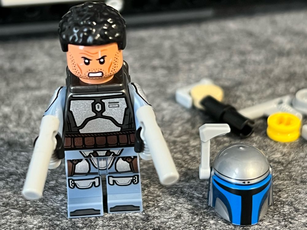 Lego Minifigur of Jango Fett looking angry with blasters in both hands. His helmet is next to him