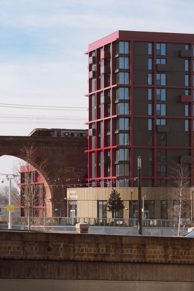 Photograph taken in Stockport from the steps alongside the Plaza theatre looking towards the railway viaduct and a new apartment building between the viaduct and the new Stockport Interchange (bus station). A CrossCountry train can be seen approaching Stockport railway station. It is a fine day with good weather.