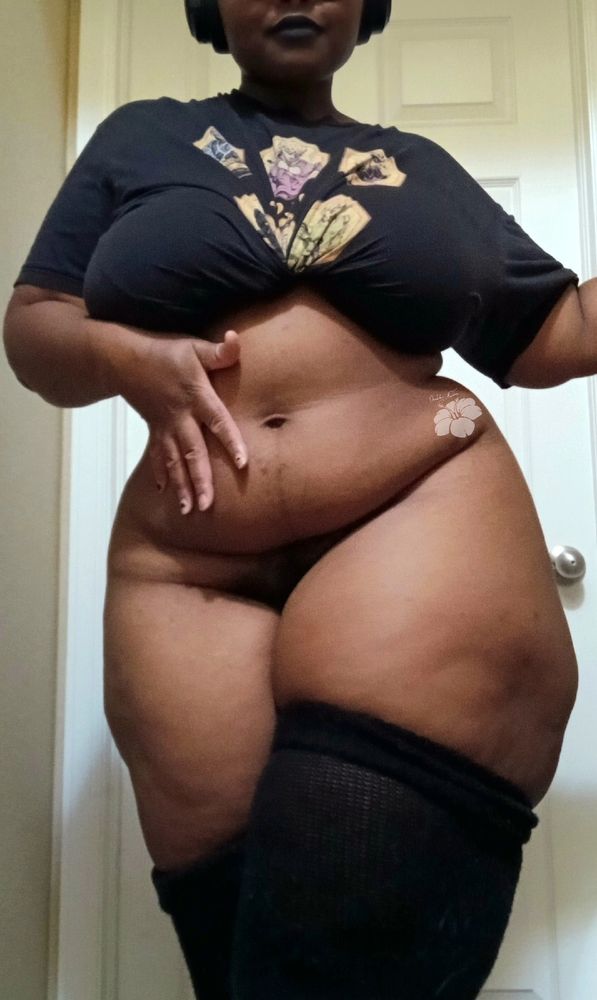 Mauve stands in front of a white door with one hand on her tummy, and the other arm extends off screen. She wears black lipstick, a black shirt tied under her breasts, and black thigh highs. She smirks at the camera.

#bbw #NsfwSky #SpicySky #ThickThursday 