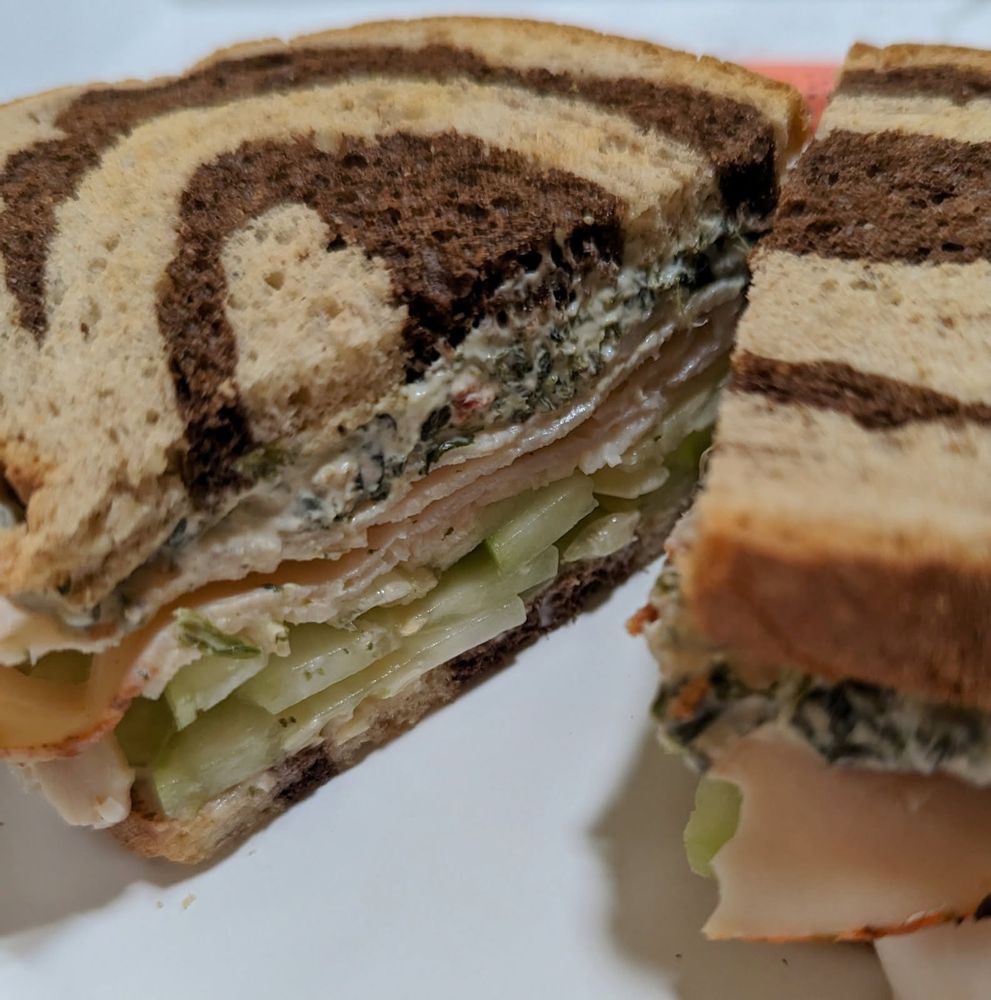 Close-up of a sandwich cut in half - peppered turkey with cucumber and spinach dip on marble rye