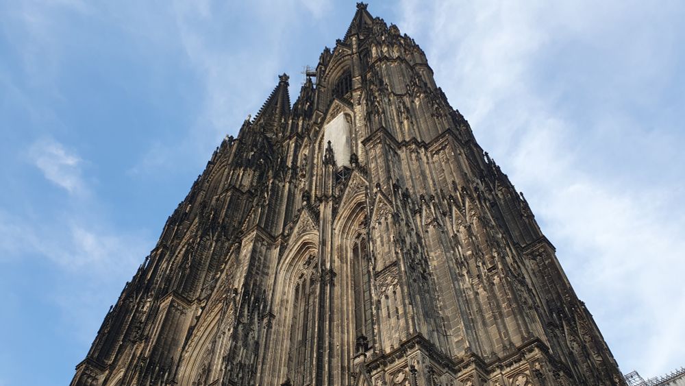 Hochsicht an den vorderen Türmen des Kölner Doms. Der Himmel ist blau und leicht bewölkt.