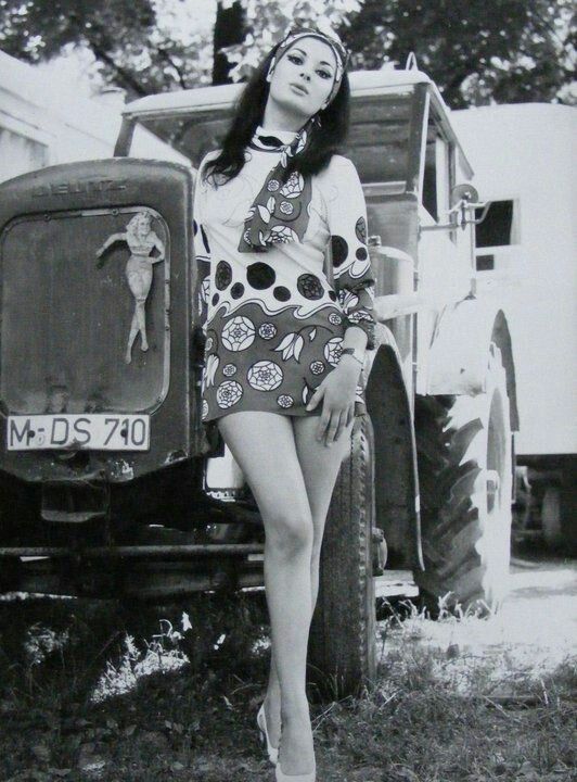 black-and-white photo of Edwige Fenech in a groovy mini-dress posing in front of a tractor that has a pinup cutout on the front of it