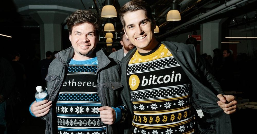 Two cryptobro dudes pulling open their jackets to reveal they are wearing sweaters that read "ethereum" and "bitcoin"