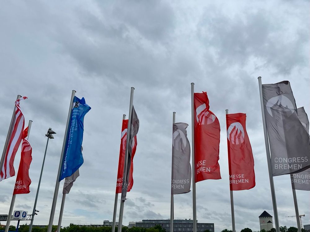 Fahnenmasten vor bewölktem Himmel mit roten, blauen und grauen Flaggen: Congress Bremen