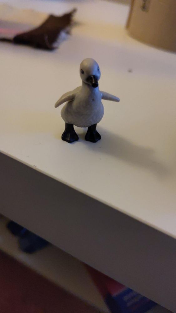 Die Babyschwanfigur aus den Überraschungseiern steht auf einem Tisch. Sie breitet die Flügel aus.