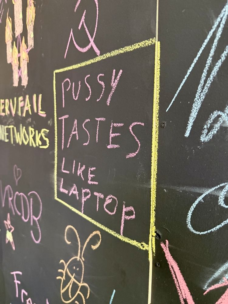 big text on chalkboard wall at GPN that says “pussy tastes like laptop”