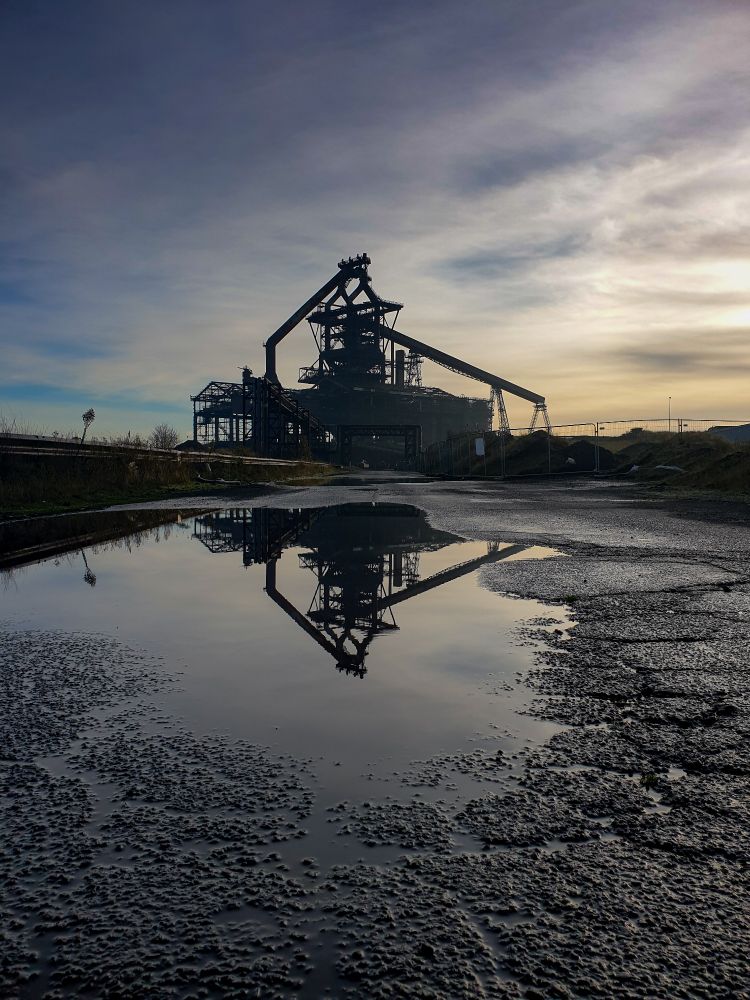 Silhouette of the Redcar blastfurnace.  Almost cleared away now, just the hearth remains.  The furnace is reflected in a roadside puddle 