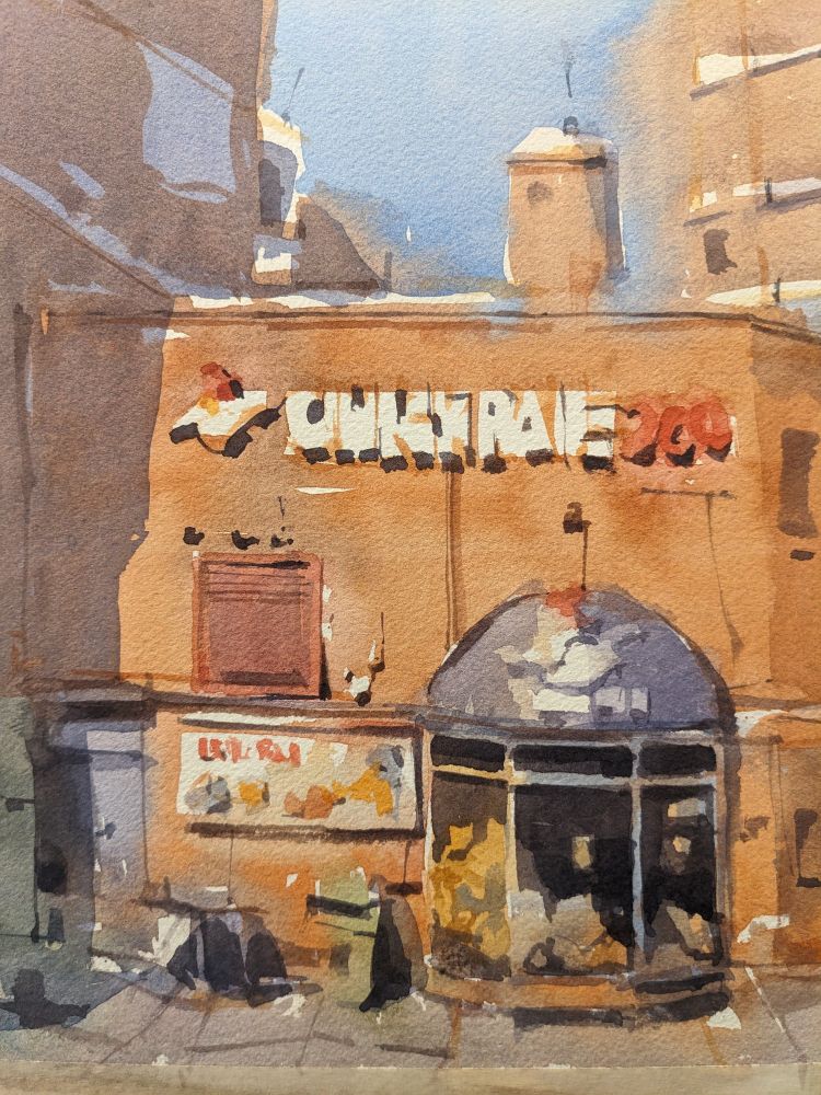 Watercolor painting of a fried chicken restaurant on the main street along the beachside resort toe of Scheveningen in The Hague. The red brick facade of the restaurant has indescript letter signage in white with a chicken logo above a ground floor entry. The ground floor has an entry to the left with a banner describing products to the left above an empty table and trash bin. To their right is a half-oval canopy with a logo hanging over tall windows revealing interior seating and additional signage. In the background, hazy buildings hem the restaurant in the frame with a blue sky in the distance.