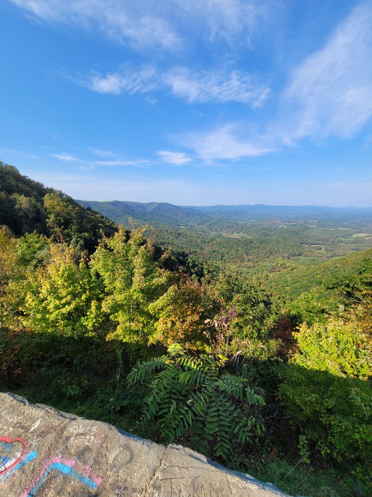 a view from on a mountain, looking over green hills and blue sky