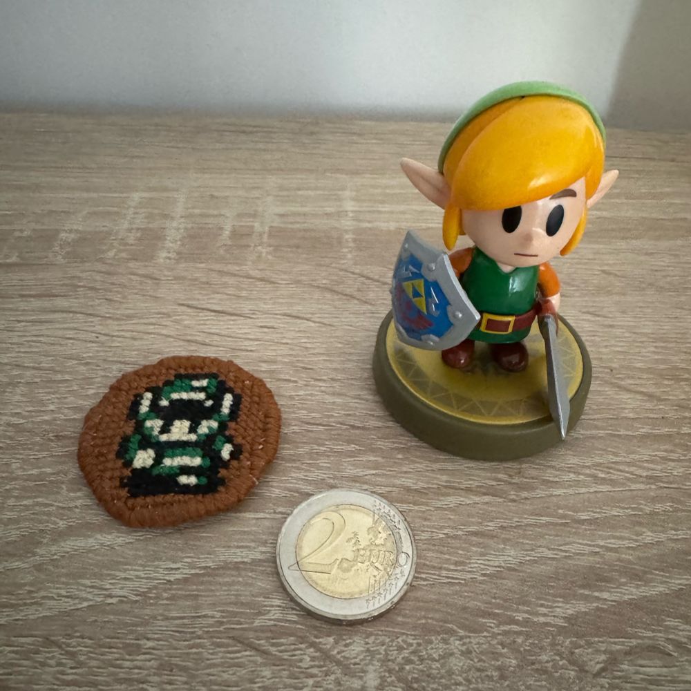 Cross stitch of Link from Link’s Awakening side by side with the Link Amiibo (from the same game) and a 2€ coin. Front side.