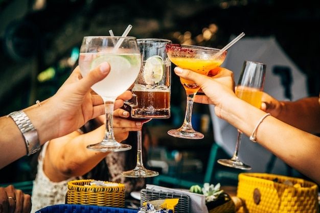 Ein Partyfoto zeigt mehrere Hände, die mit bunten  Cocktails anstoßen.