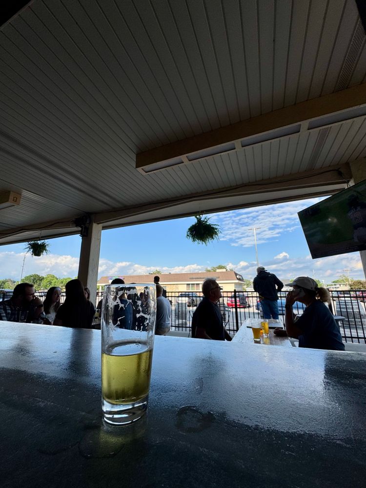 a half-consumed beer on a stone-slab bar top overlooking an open-air patio. a marcos pizza looms in the background