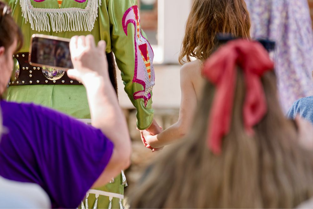 A Native American jingle dancer holding hands with a young girl in a dance circle