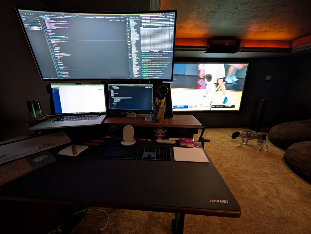 Work screens at stand-up desk with a big screen playing March Madness in the background
