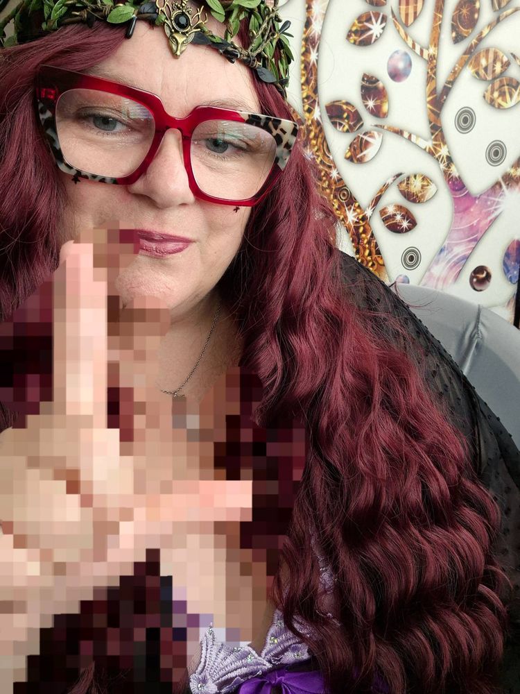 A velvet-draped queen, I lounge in my finery, the delicate curves of my fingers forming the loser sign as I taunt you with a glimpse of my pampered skin, my crown a whispered promise of the pleasures that lie beyond your reach.