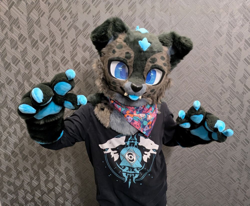 A waist-up photo of a person wearing a partial fursuit of a Godzilla-inspired dog standing in a hotel hallway. The character is dark gray with spotty markings, floppy ears, and bright blue accents. 